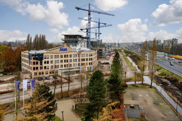 Luchtfoto van de Burgemeester Rijnderslaan in Amstelveen met het Atos-gebouw, bouwkranen en de naastgelegen snelweg.